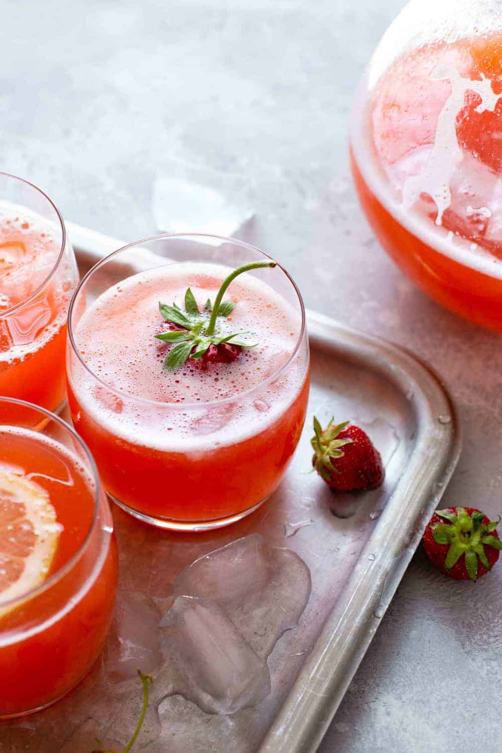 Glasses of strawberry lemonade next to a pitcher of strawberry lemonade