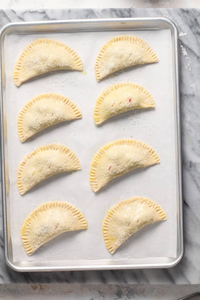 Assembled cherry hand pies on a parchment-lined baking sheet, ready to be baked