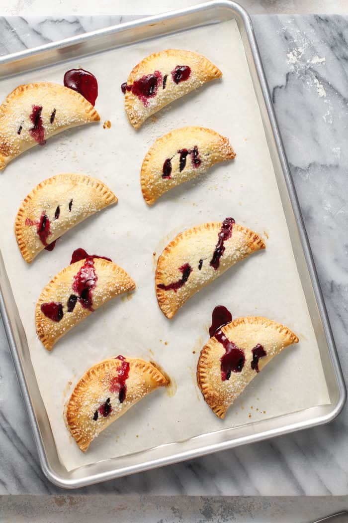 Baked cherry hand pies cooling on a parchment-lined baking sheet