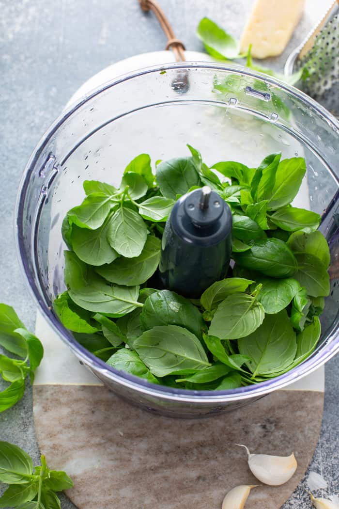 Fresh basil leaves in the bowl of a food processor