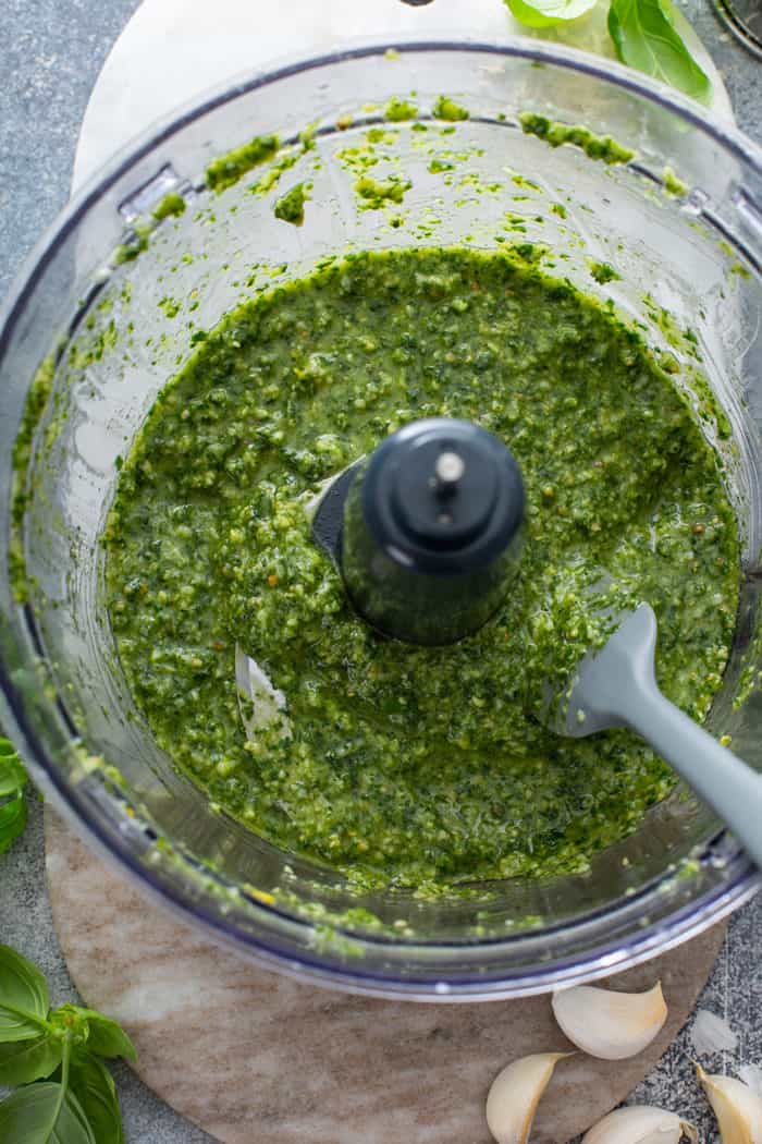 Spatula stirring basil pesto in the bowl of a food processor