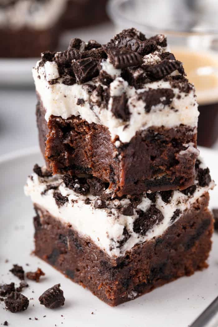 Two oreo brownies stacked on a white plate. A bite has been taken out of the corner of the top brownie.