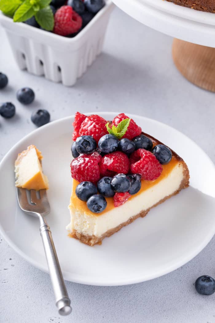 Fork taking a bite from a slice of ricotta cheesecake on a white plate.