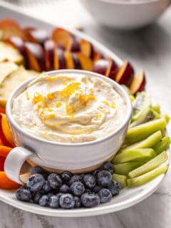 Bowl of orange fruit dip set on a platter of fresh fruit