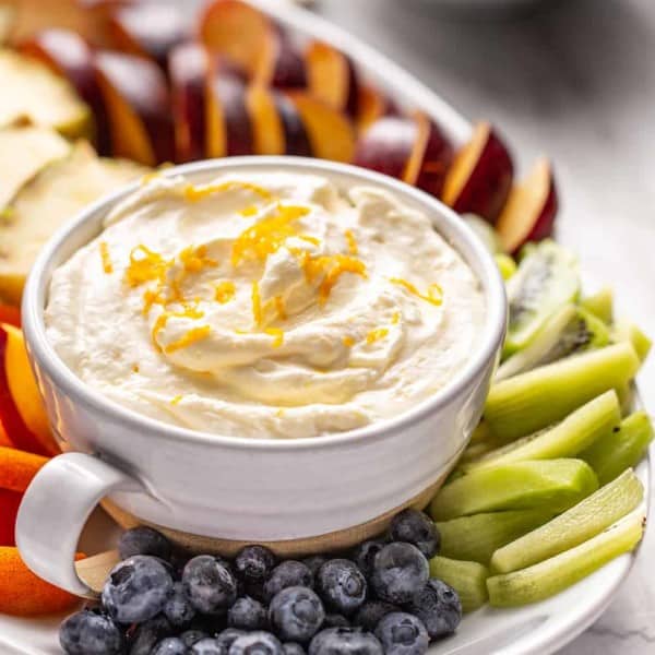 Bowl of orange fruit dip set on a platter of fresh fruit