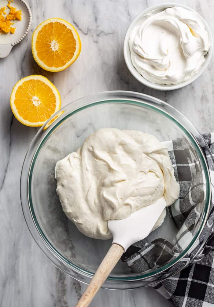 Spatula stirring together cream cheese and powdered sugar for fruit dip in a glass mixing bowl
