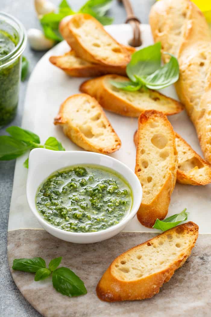 Small bowl of basil pesto surrounded by slices of baguette