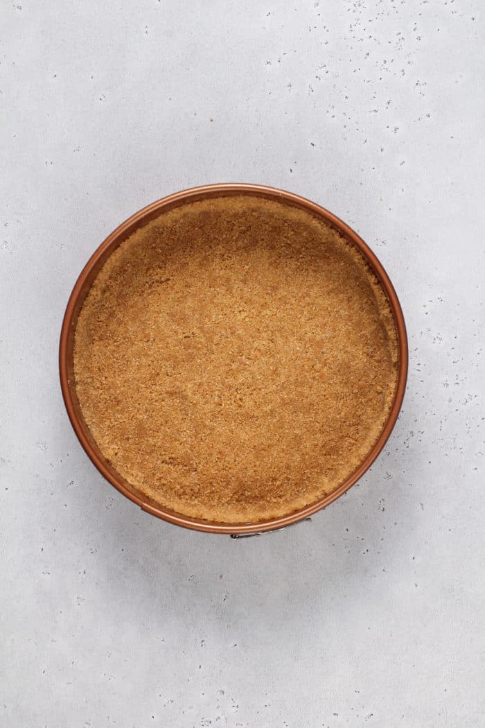 Graham cracker crust in a springform pan on a gray countertop.