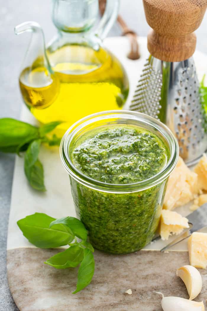 Glass jar filled with basil pesto on a cutting board