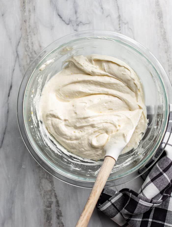 Spatula stirring together orange fruit dip in a glass bowl on a marble countertop