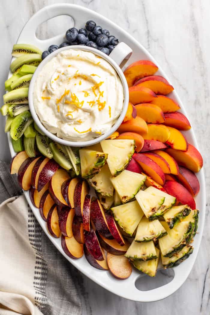 Overhead view of a bowl of orange fruit dip on a platter filled with assorted fresh tropical fruits