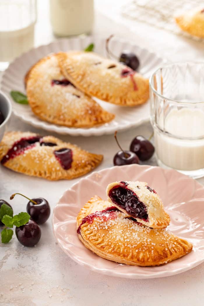Cherry hand pies on two plates. One of the hand pies is cut in half to show the filling
