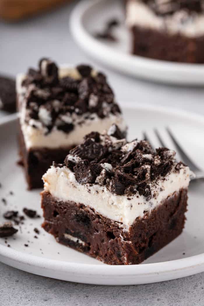 Close up of two oreo brownies topped with frosting and chopped oreos on a white plate.