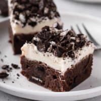 Oreo brownie topped with vanilla frosting on a white plate.