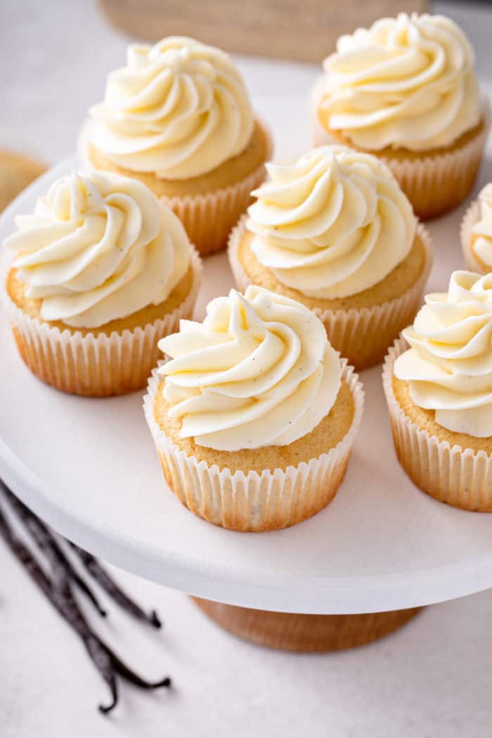 Several vanilla cupcakes topped with vanilla frosting on a white platter.