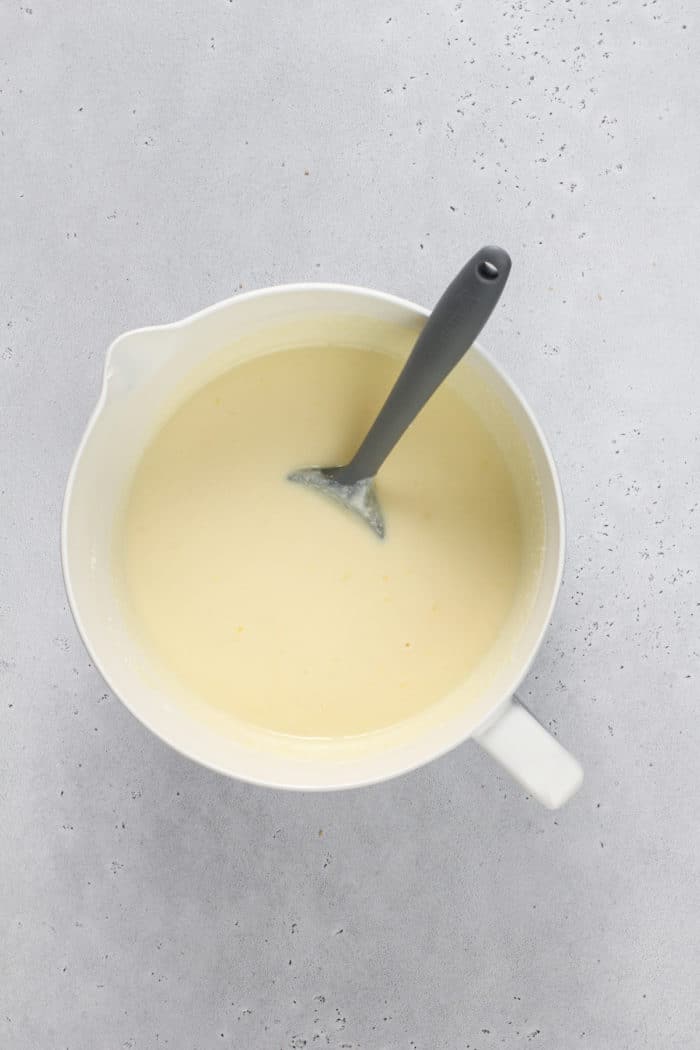 Batter for ricotta cheesecake being stirred with a spatula in a white mixing bowl.