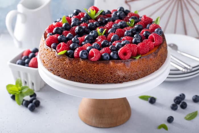 Ricotta cheesecake on a cake stand, topped with rows of raspberries and blueberries.