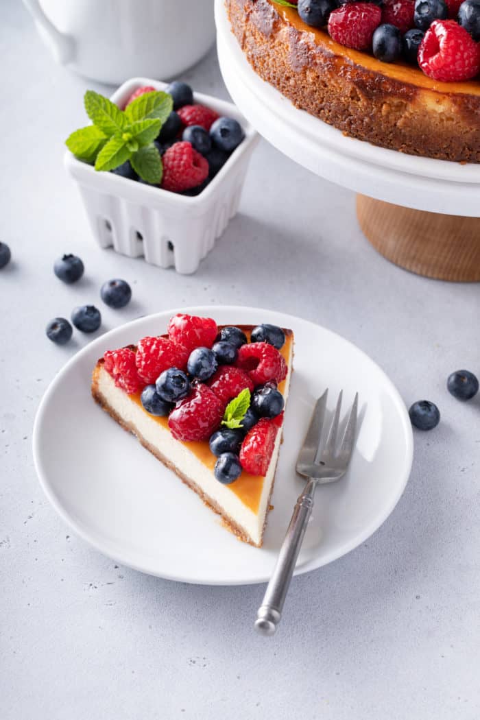 Slice of ricotta cheesecake topped with red and blue berries on a white plate.