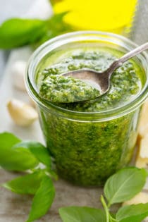 Spoon taking a spoonful of basil pesto out of a glass jar