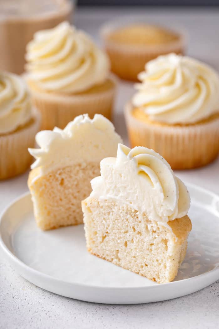 Unwrapped vanilla cupcake cut in half on a white plate.