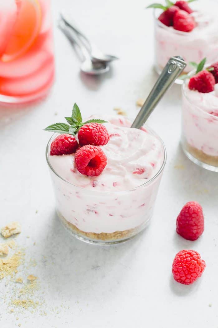 Bowl of no-bake raspberry lemon cheesecake with a spoon in it. There are more dishes of cheesecake in the background