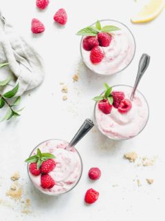 Overhead view of three bowls of no-bake raspberry lemon cheesecakes garnished with fresh raspberries and mint on a marble countertop