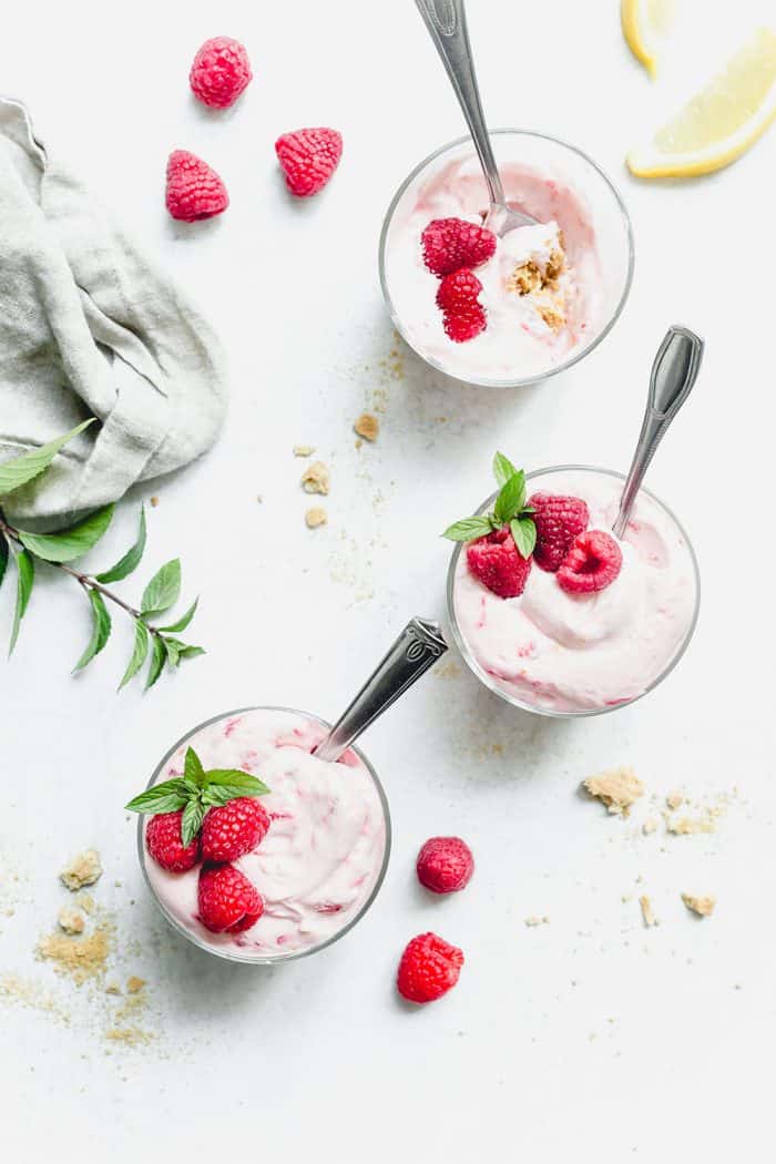 Three glass dishes of no-bake raspberry lemon cheesecake on a marble counter. There is a spoon in each dish