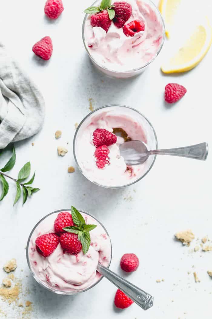 Three bowls of no-bake raspberry lemon cheesecakes on a marble countertop. The middle bowl is partially eaten with a spoon still in it