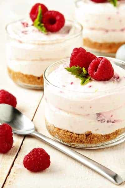 Raspberry lemon no bake cheesecake in a small glass container next to a spoon and fresh raspberries