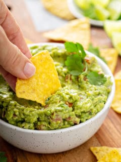 Hand dipping a tortilla chip into a bowl of spicy guacamole