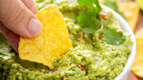 Hand dipping a tortilla chip into a bowl of spicy guacamole