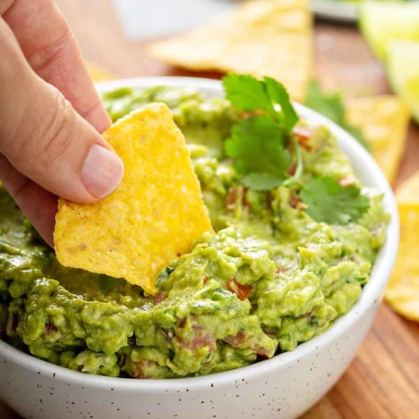 Hand dipping a tortilla chip into a bowl of spicy guacamole