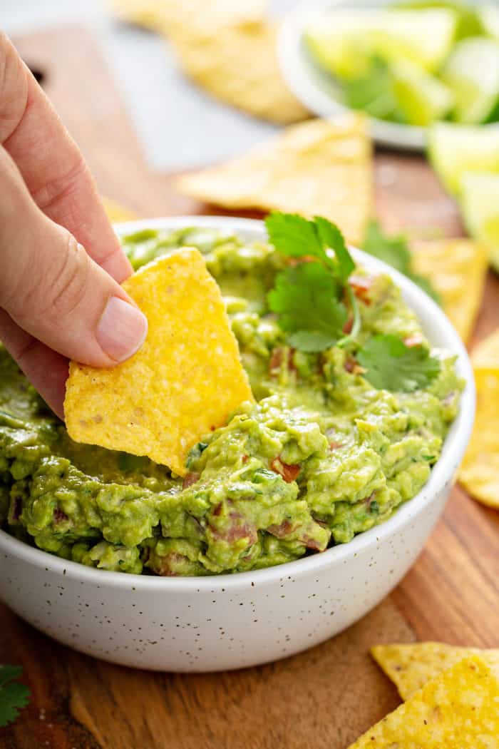 Hand dipping a tortilla chip into a bowl of spicy guacamole