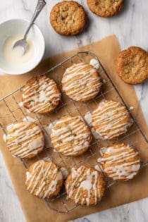 freshly glazed zucchini cookies on a wire rack over a piece of parchment paper. A bowl of glaze and unglazed cookies are next to the rack