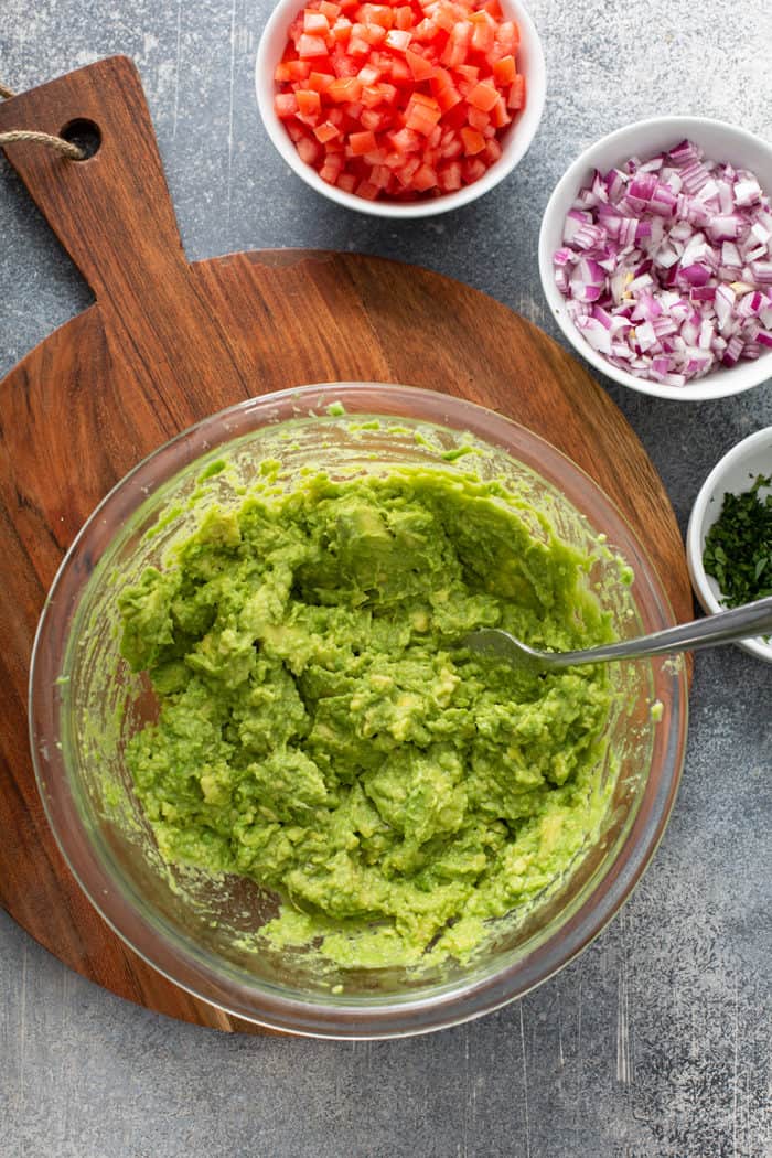 Fork mashing together avocado and lime in a glass mixing bowl