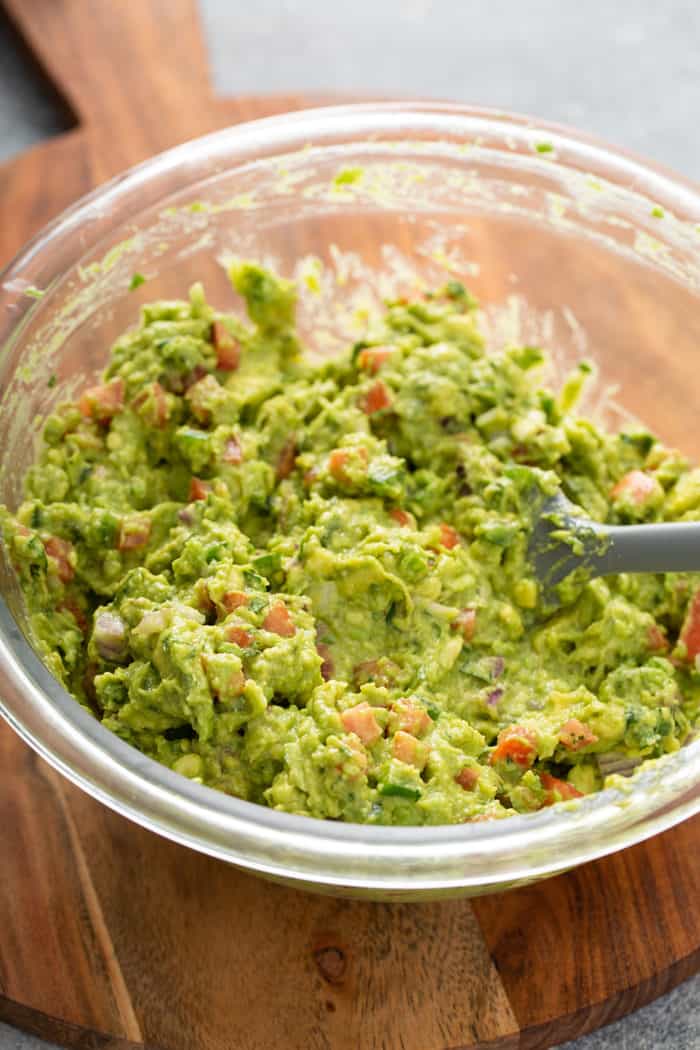 Spatula stirring spicy guacamole in a glass mixing bowl