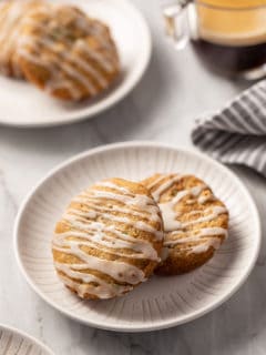 Two white plates on a marble countertop, each holding two zucchini cookies