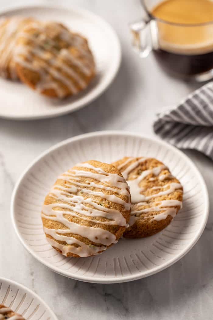 Two white plates on a marble countertop, each holding two zucchini cookies