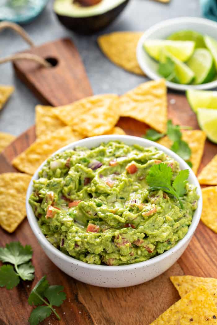 White bowl filled with spicy guacamole set on a wooden board, surrounded by tortilla chips