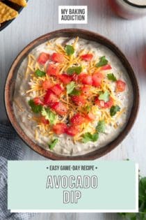 Overhead view of a bowl filled with avocado dip, garnished with shredded cheese, diced tomatoes, and cilantro. Text overlay includes recipe name.