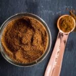 Overhead view of a glass jar full of pumpkin pie spice next to a measuring spoon on a stone surface