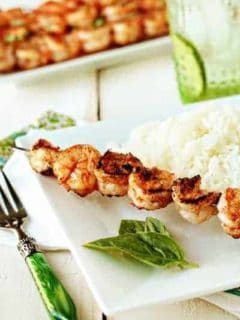 Marinated grilled shrimp on a skewer next to white rice on a plate