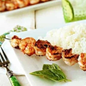 Marinated grilled shrimp on a skewer next to white rice on a plate