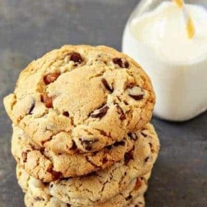 A stack of turtle cookies in front of a glass of milk of a stone surface