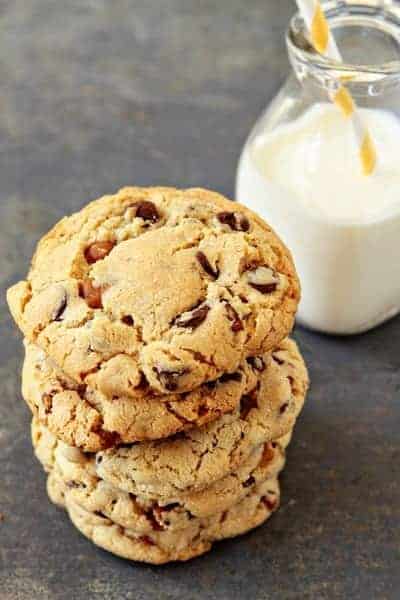 A stack of turtle cookies in front of a glass of milk of a stone surface