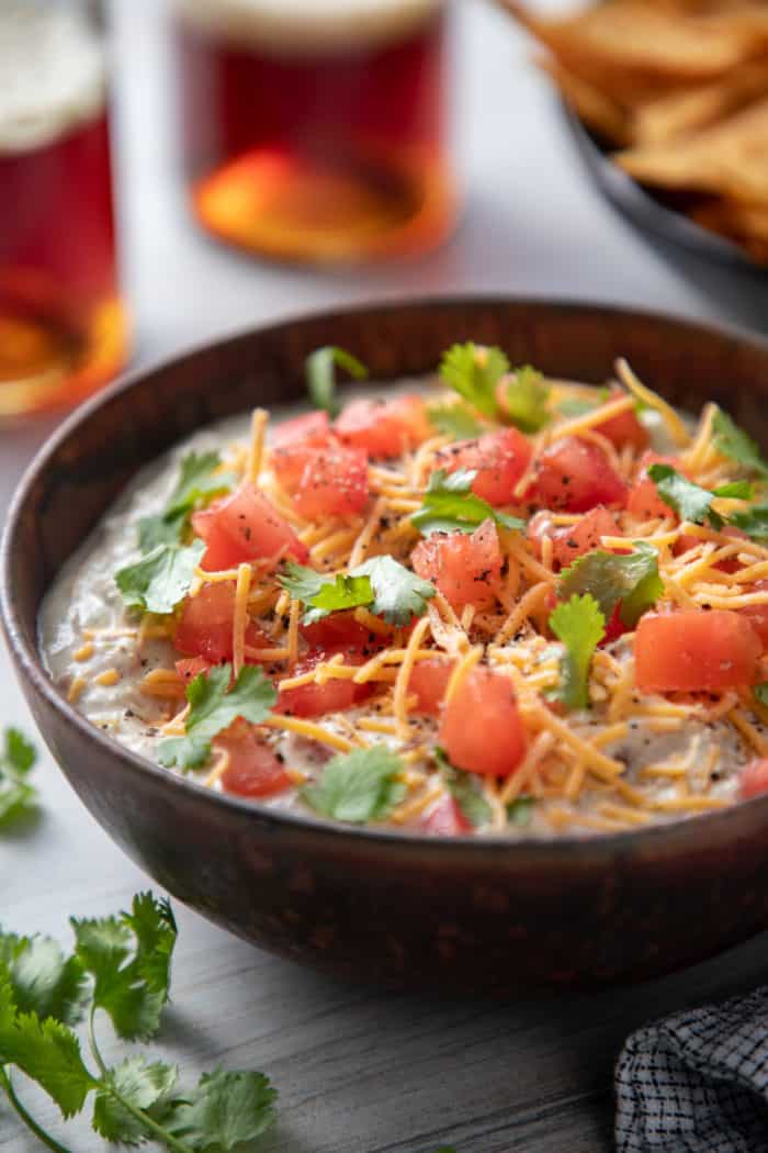 Brown bowl filled with avocado dip that has been garnished with tomatoes, cheese, and cilantro.