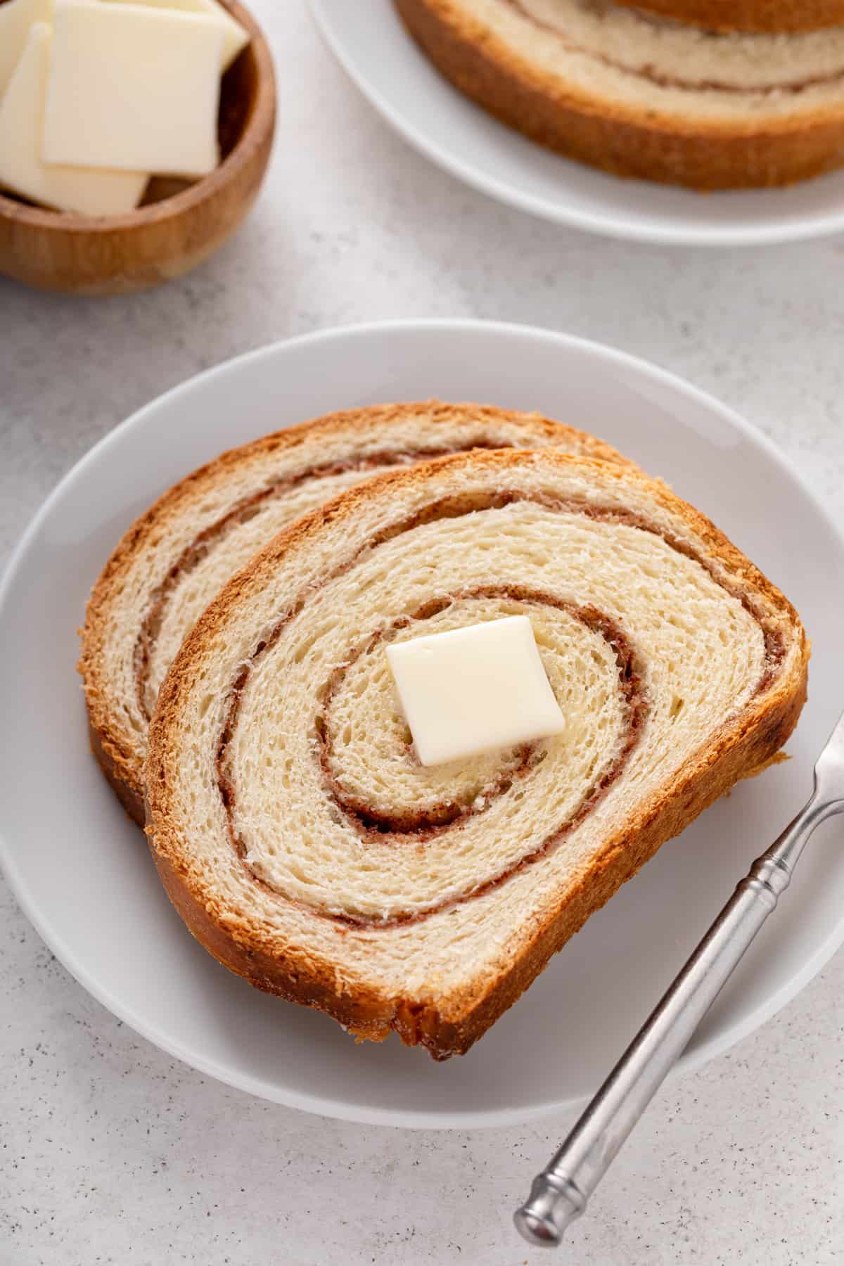 Close up of two slices of cinnamon swirl bread topped with a pat of butter on a white plate.