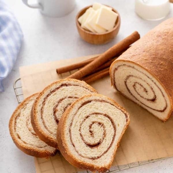 Three slices of cinnamon swirl bread on a piece of parchment paper next to the rest of the loaf.