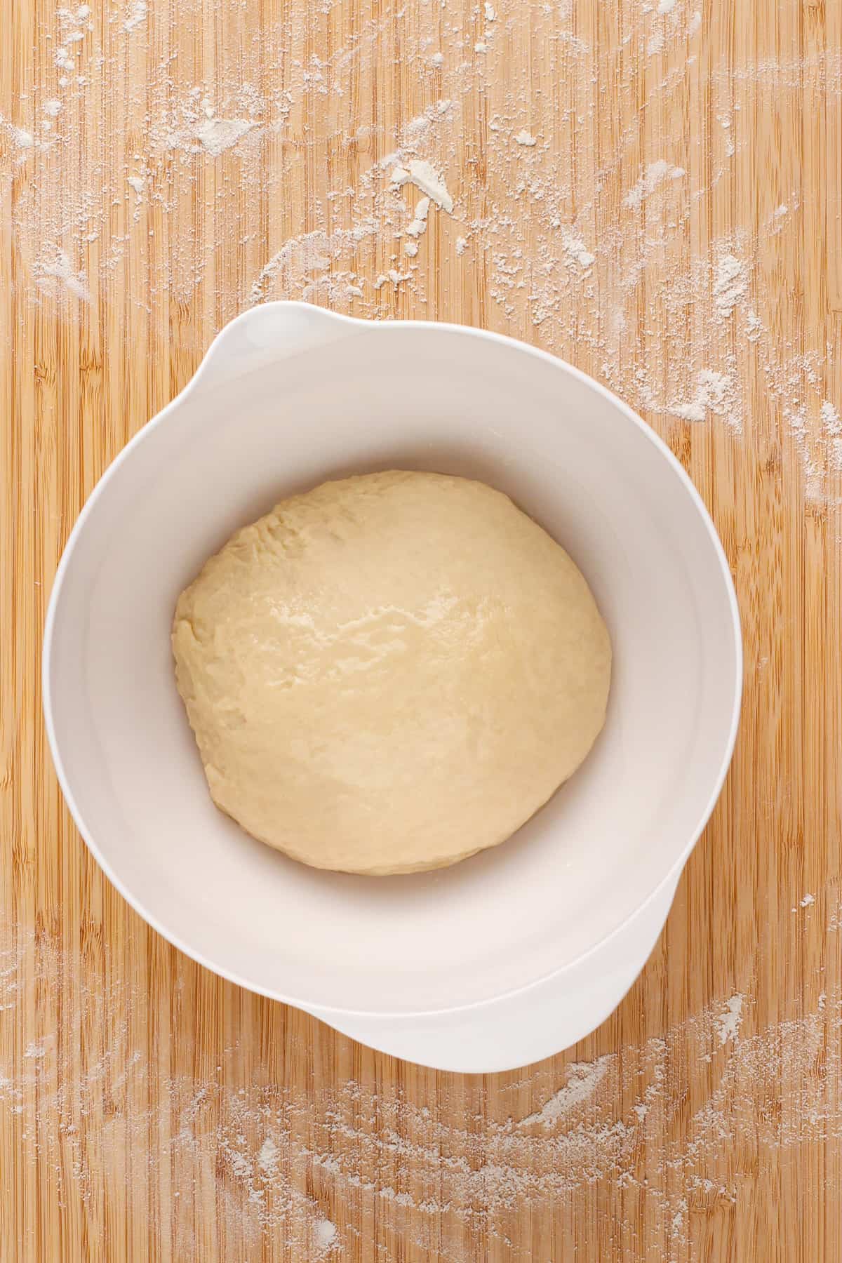 Kneaded bread dough in a white bowl, ready to rise.