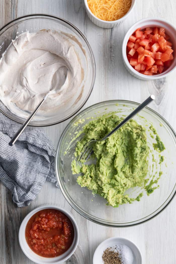 Bowl of avocado mash next to a bowl of mixed sour cream and cream cheese.